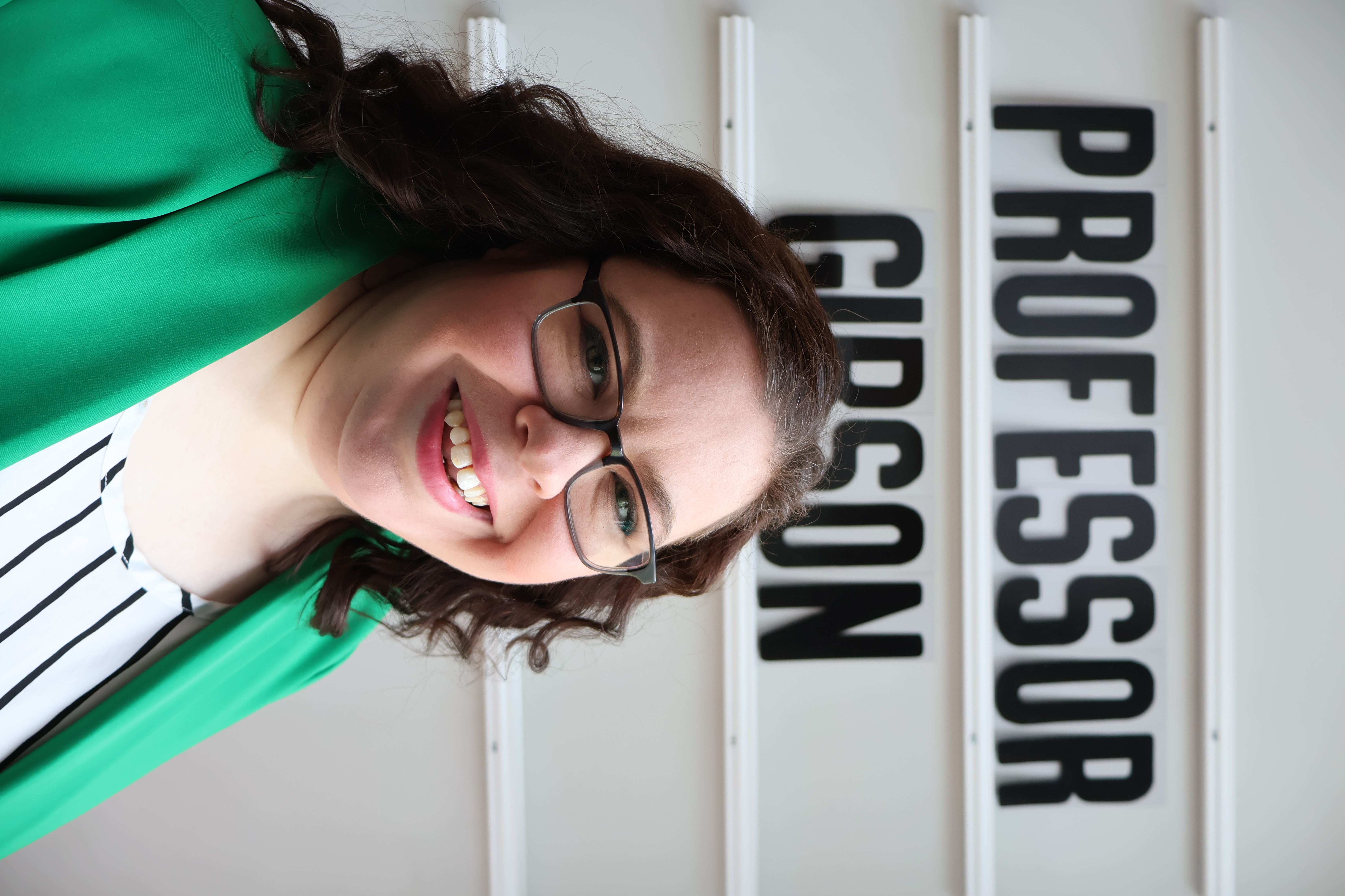 Sarah Gibson Headshot. Sarah smiling in front of a black and white background.